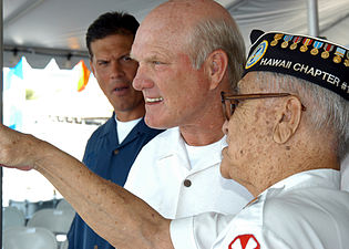 Un capitaine de la Navy pointe au loin, montrant un élément à une personne à laquelle il parle.