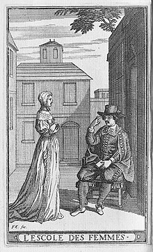 Une femme debout, de profil, devant un homme assis.