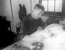 Image en noir et blanc montrant le dessinateur à sa table à dessin.