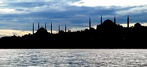 Silhouette of several buildings with domes and spires in front of an open waterway at twilight