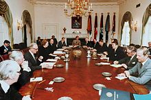Thatcher adalah satu-satunya wanita di ruangan ini, dan selusin pria dalam setelan duduk di sekitar meja oval. Regan dan Thatcher duduk berlawanan satu sama lain di tengah-tengah meja panjang. Ruangan ini dihiasi dengan cat warna putih, dengan tirai, sebuah lampu emas dan potret Lincoln.