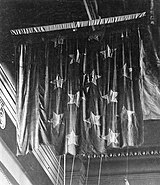 Czarno-białe zdjęcie z roku 1914 przedstawiające pociętą kulami banderę zawieszoną pod sufitem muzeum