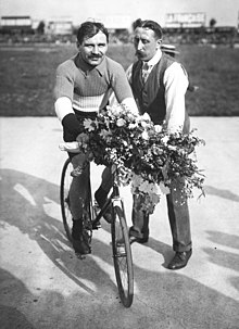 Cycliste sur son vélo, portant une gerbe de fleurs.