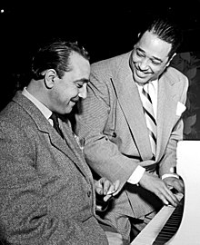 Deux hommes assis devant un piano blanc. Ellington a les mains sur le clavier, Django fume une cigarette