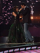 A man dressing a black suit and jeans and a woman sporting a black dress performing on a stage.