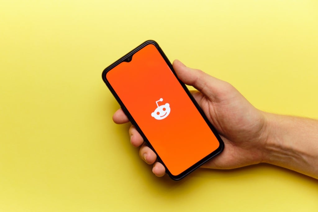 A smartphone displays the Reddit logo and name on an orange gradient background, resting on a laptop keyboard