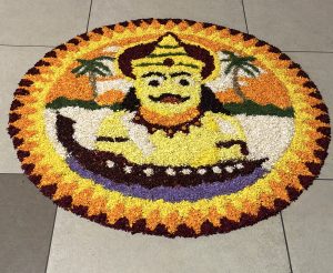 A colorful circular floral arrangement featuring a deity with a yellow face and ornate headdress, surrounded by orange and yellow petals.